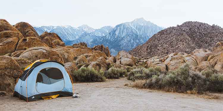 A three-season tent set up in a rocky dessert area with mountains in the background.