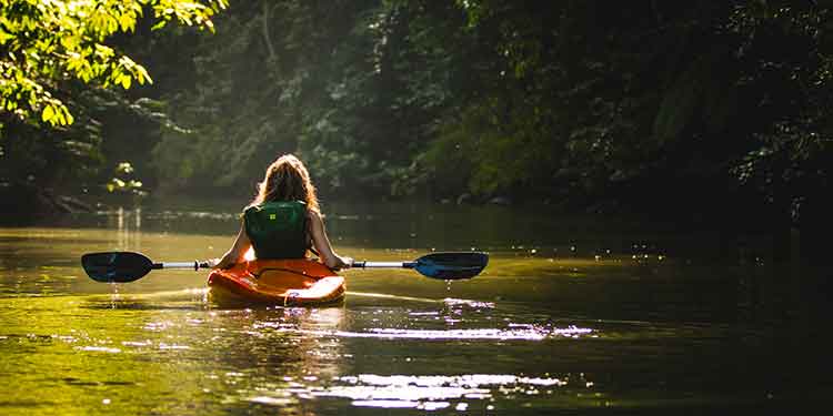 A female kayaker wearing appropriate safety equipment on a slow moving river.