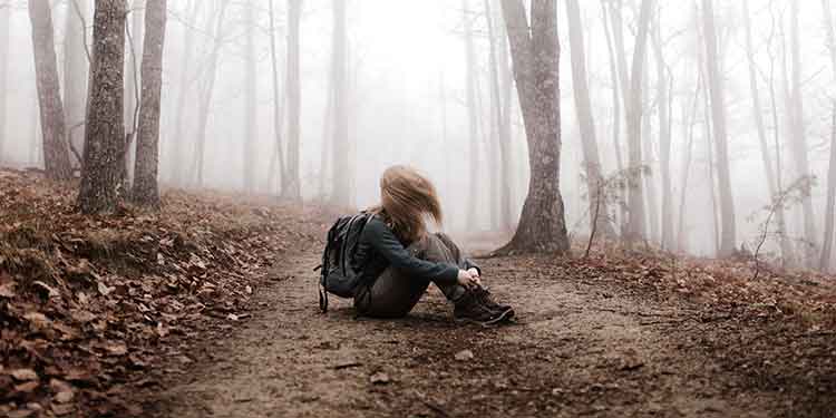 A female hiker in distress sits on a creepy hiking trail.