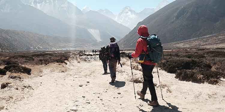 A group of backpackers using trekking poles hike through a rocky valley between ominously tall mountains.