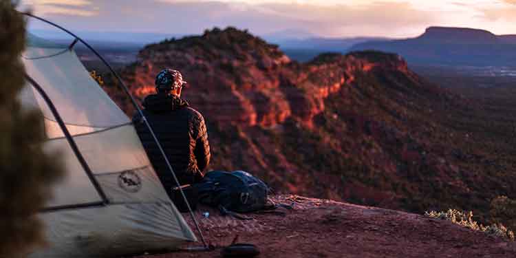 Camper sitting in front of his tent watching the sunset over a canyon.