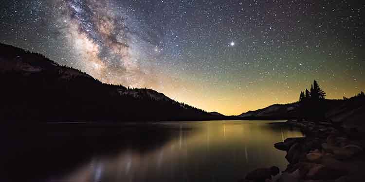 Night hiking scene of mountains and a lake under the Milky Way.