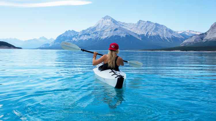 Woman with a low angle paddling style and properly adjusted drip rings in an Oru Kayak kayaking on a lake with mountains miles in the distance.