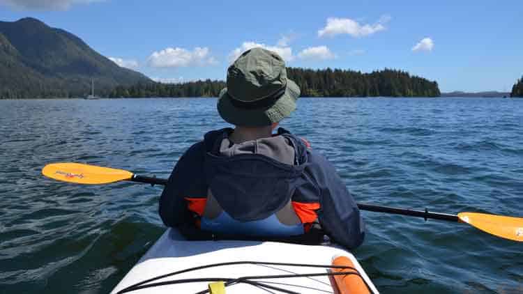 Kayaker paddling on a large lake with properly set kayak paddle drip guards.