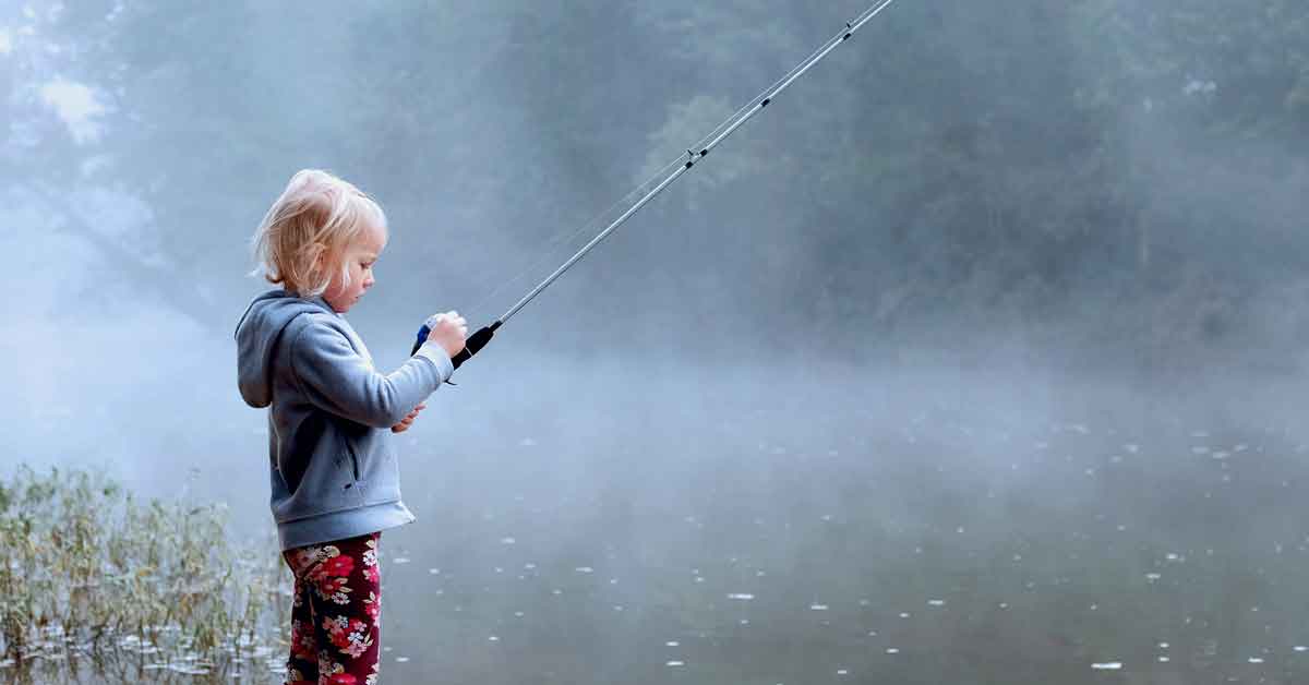 A little girl learning how to fish with a rod and reel combo at a lake on a foggy morning.