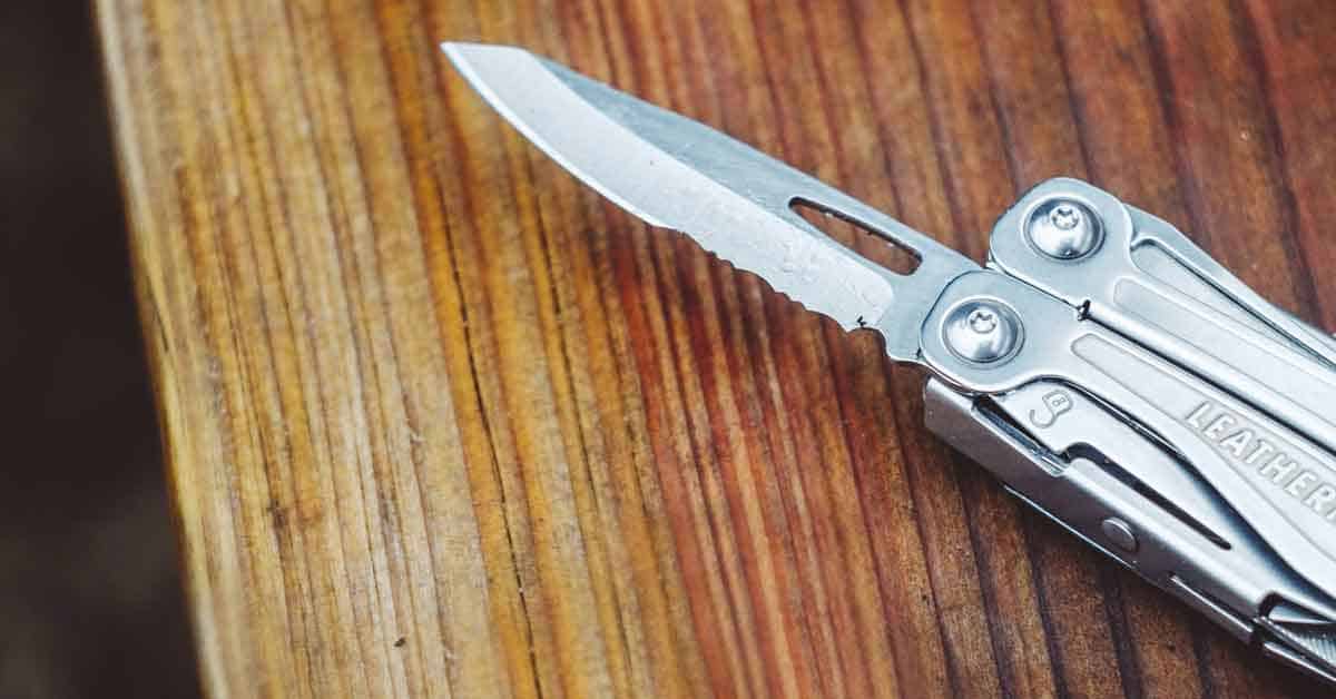 Leatherman multitool laying on a plank of wood with knife blade open.
