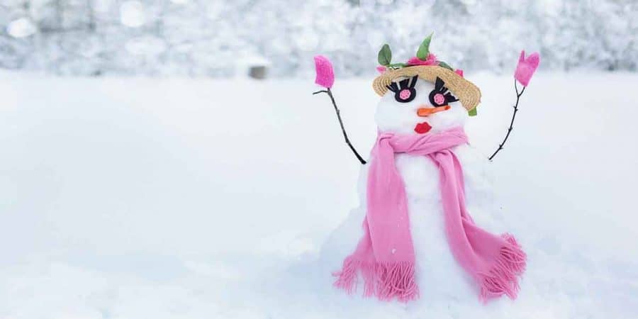 A snowman or rather snowwoman with a flowery hat with pink roses, pink eyes, eyelashes, carrot nose, red lips, pink mittens, and pink scarf.