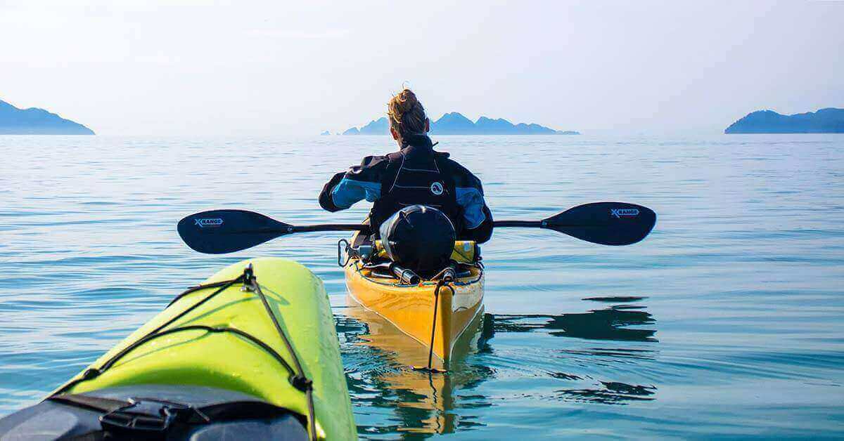 Kayaking in a drysuit to keep warm in cold weather with a dry bag packed with extra gear on the stern of the kayak..