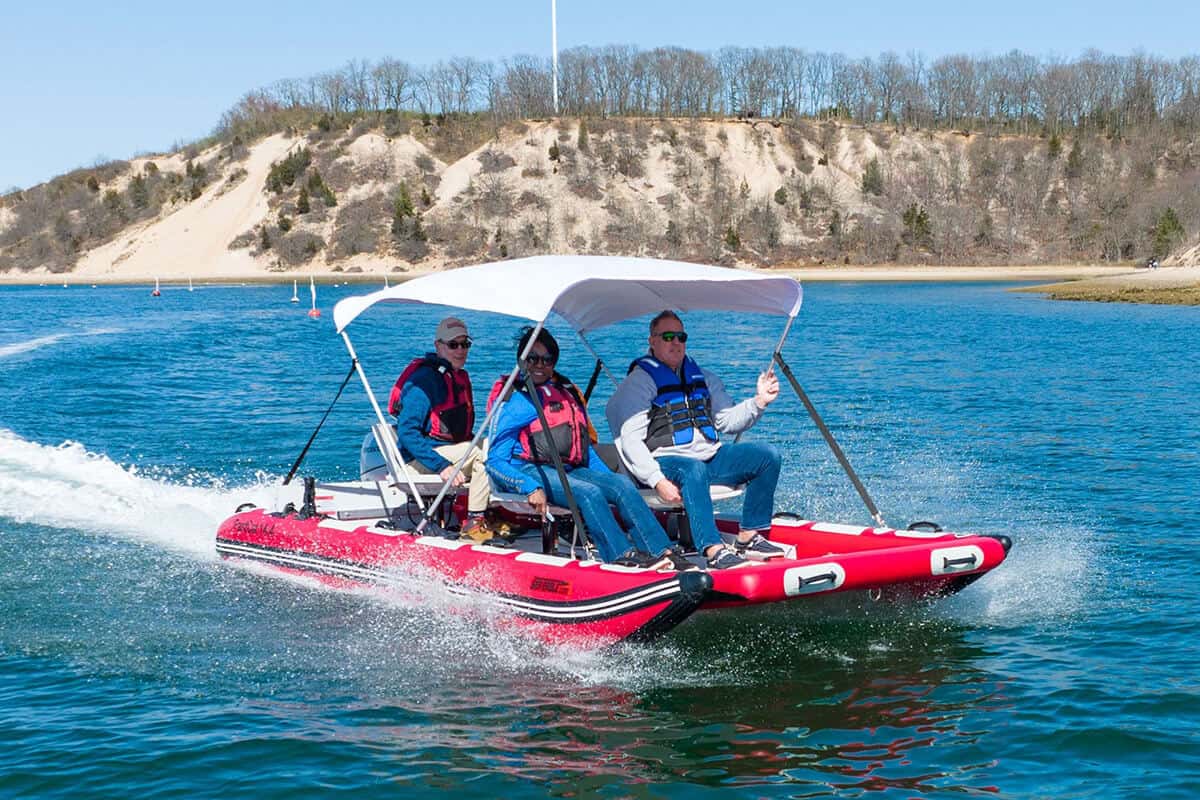 A Sea Eagle FastCat14 Catamaran Inflatable Boat with a canopy and four adults powering over the water of a large lake.