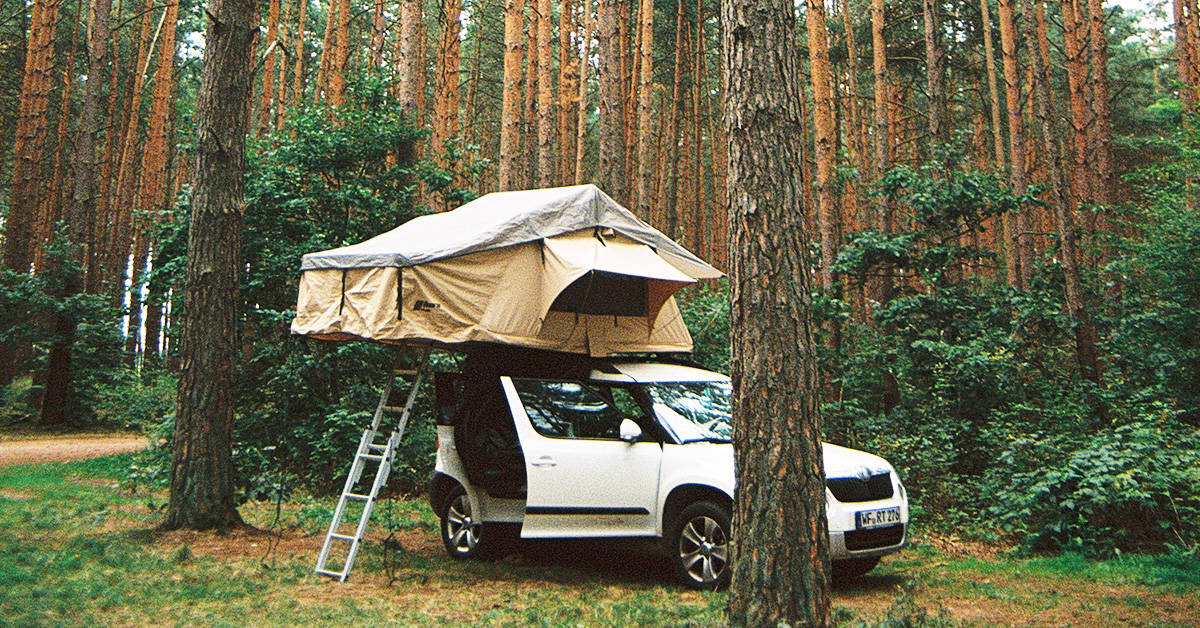 A soft shell roof top tent installed on a small SUV in the woods.