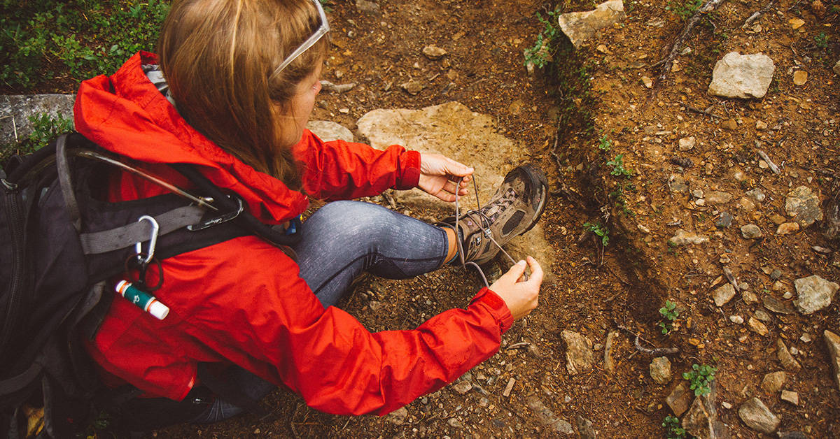 Hiker lacing up hiking boots what will protect her ankles and provide cushion and support for her knees.