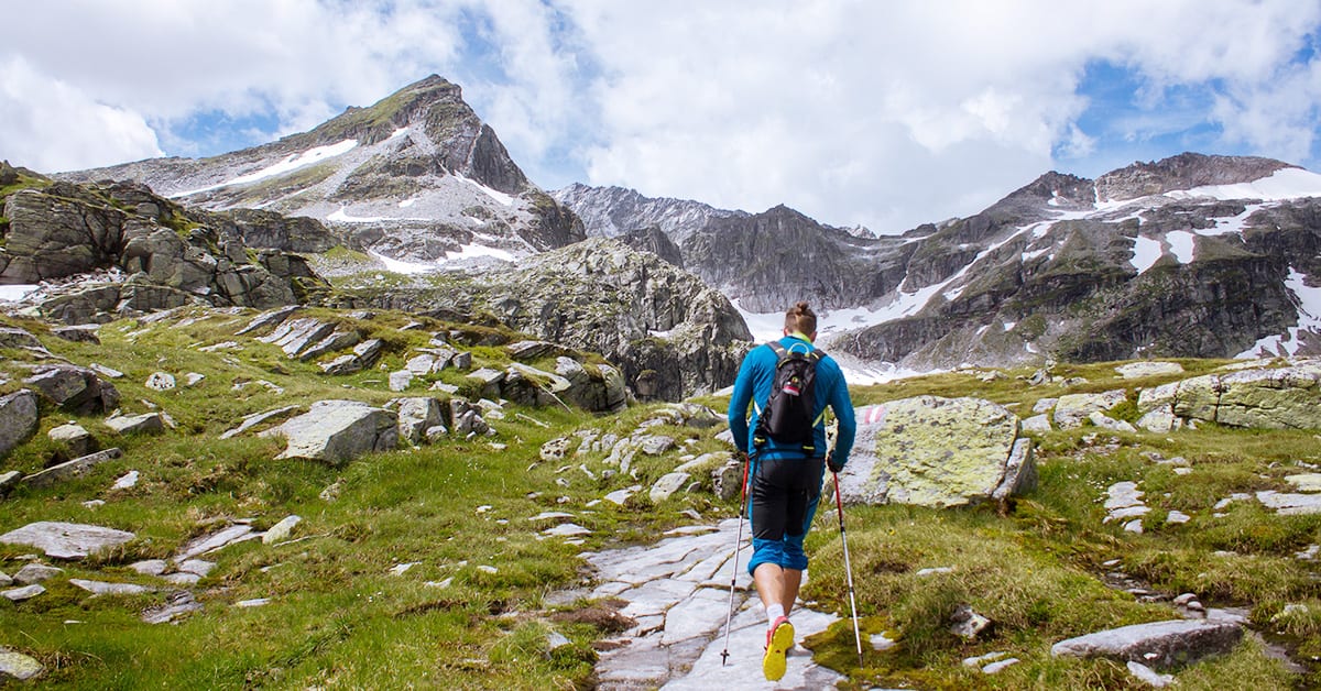 A hiker using trekking poles on a rocky trail in the mountains. Trekking poles improve knee protection for hiking.