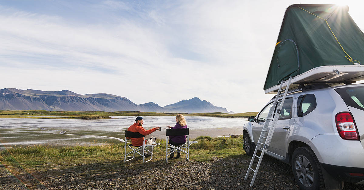 A couple drinking coffee on a cold morning outside their hard shell rooftop tent.