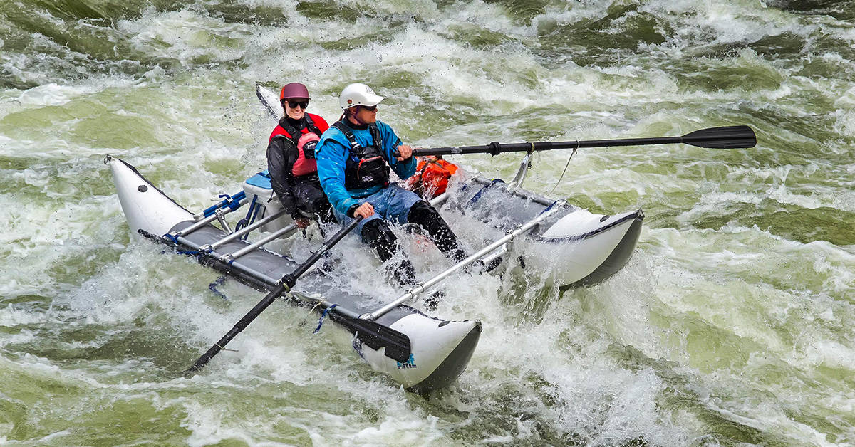 Two people on an Aire cataraft on a whitewater river.