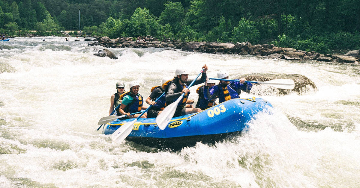 Seven people including the guide on an NRS paddle raft on a whitewater river.