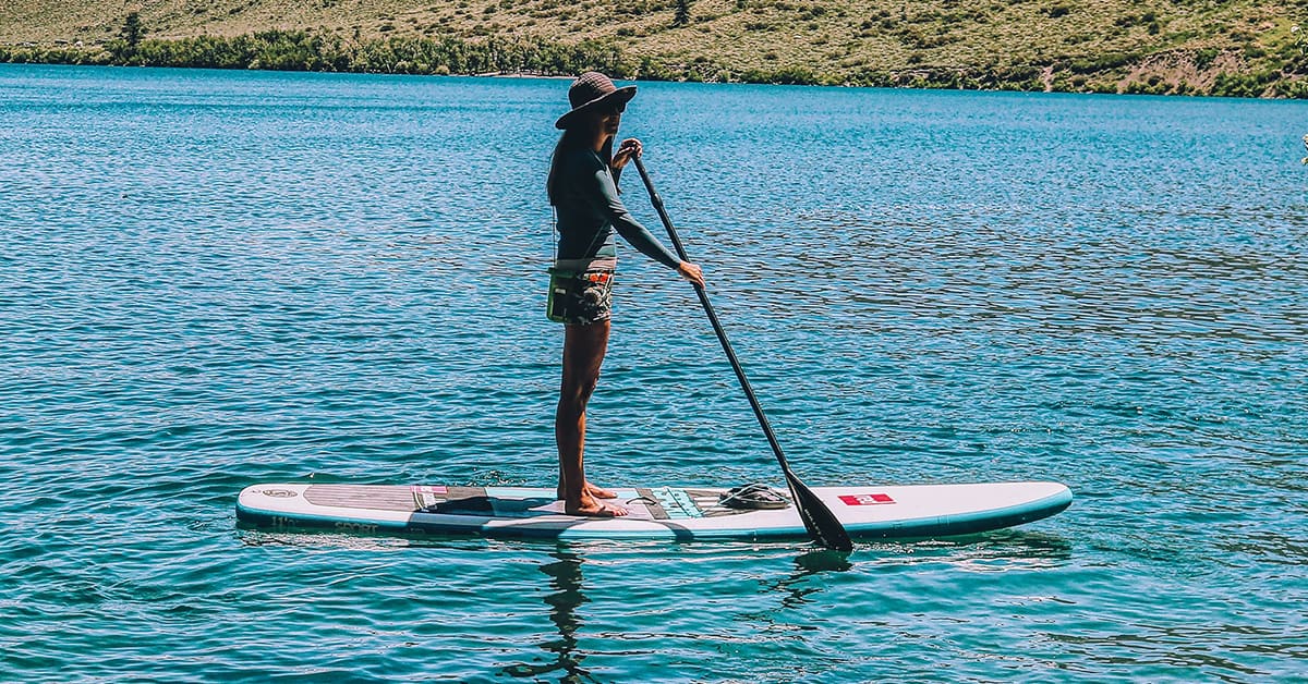 Woman paddling a Red Paddle Co inflatable SUP on a large lake.