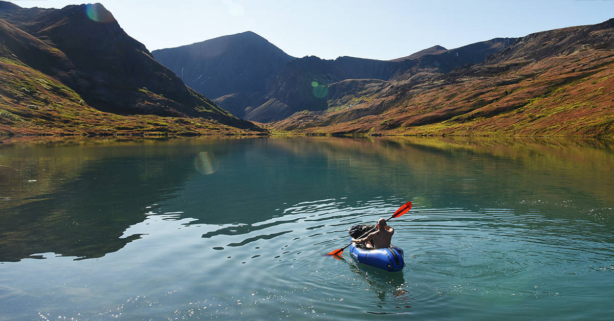 A man paddling a packraft down a calm river in the mountains.