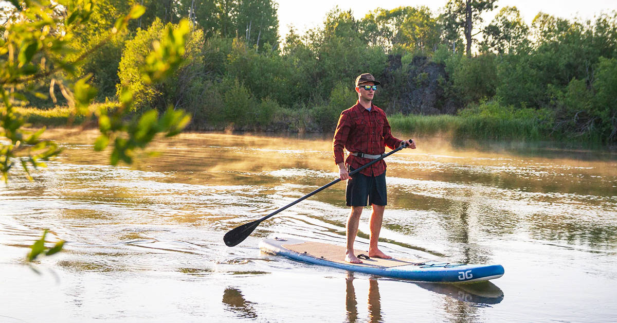 A man paddling an Aquaglide Cascade 11 inflatable SUP paddleboard down a slow-moving river.