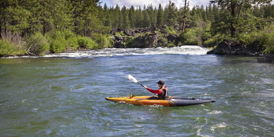 Female kayaker paddling a Aquaglide Deschutes 110 inflatable kayak on a scenic river.