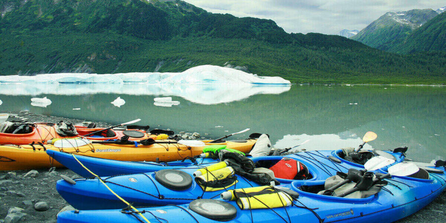 Five 2-person touring kayaks on the shore of a lake front of an iceberg in Chugach National Forest, Anchorage, AK, USA.