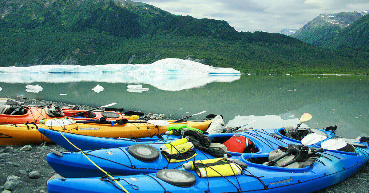 Five 2-person touring kayaks on the shore of a lakefront of an iceberg in Chugach National Forest, Anchorage, AK, USA.