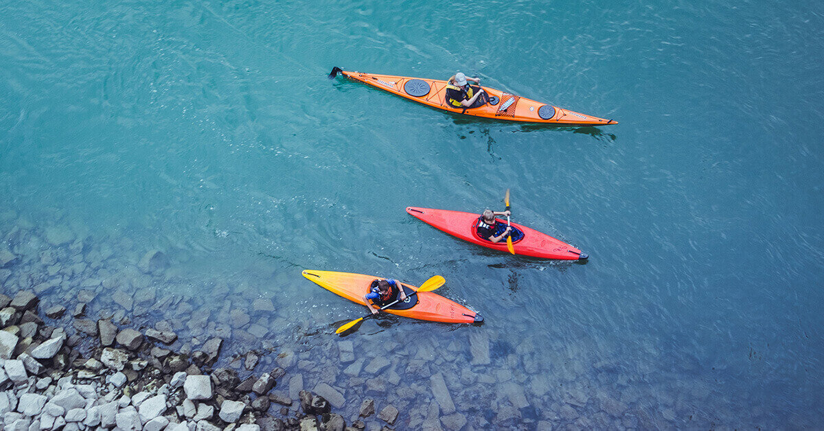 A group of three kayakers takes a paddling break near a rocky shoreline.
