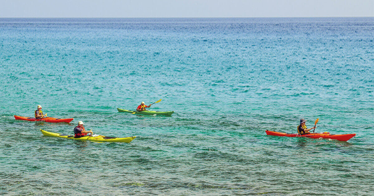 Four kayakers paddling in a group on open water.