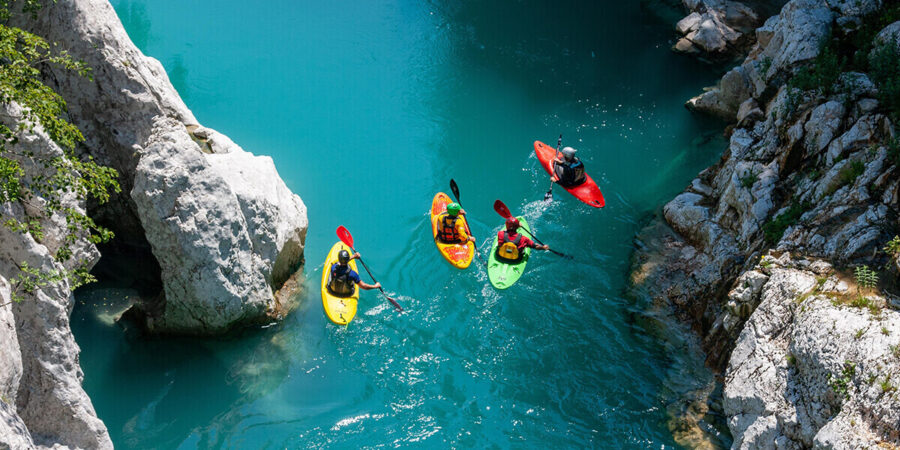 A group of four kayakers in whitewater kayaks paddling along an area of slow moving water in a ravine.