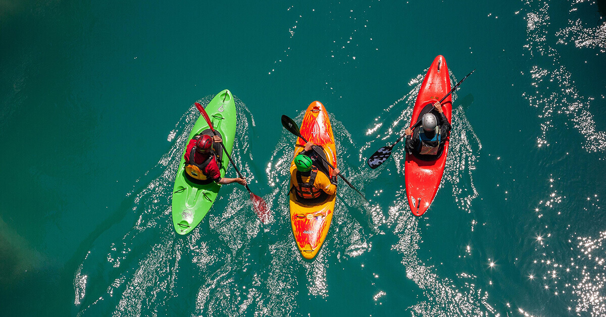 A group of three whitewater kayakers paddling together.