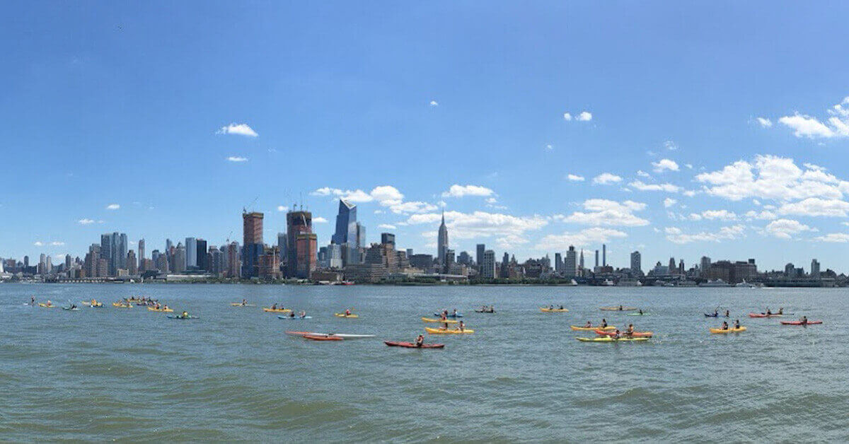 A panoramic view of a kayak group in a paddling event on the Hudson River with New York City as the backdrop.