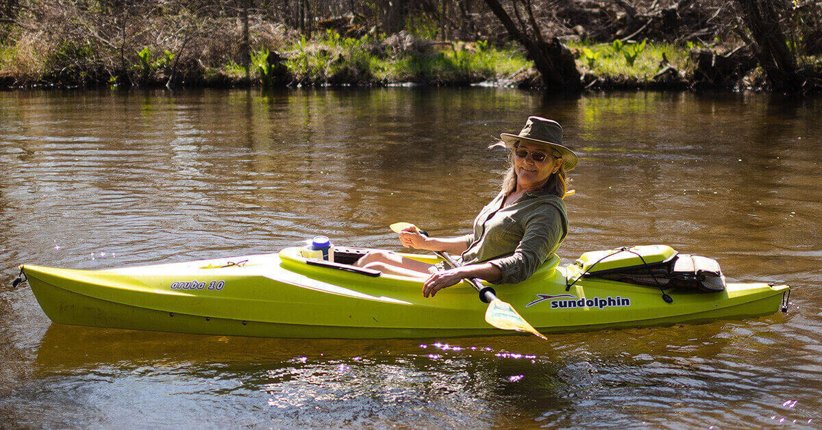 A female kayaker on a lazy river with a can of beer in the drink holder.