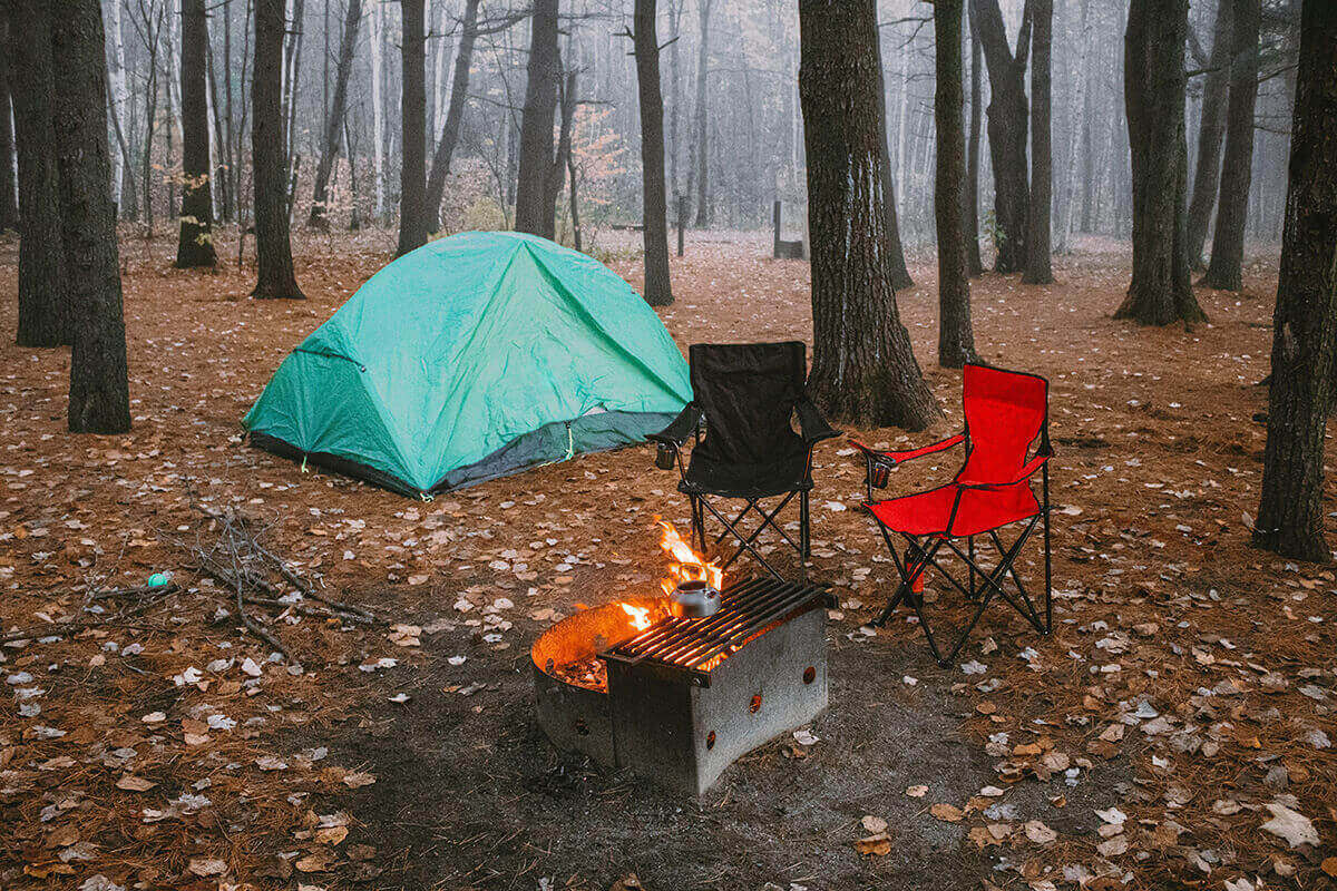 A tent set up next to a firepit at a campground on a cold fall day.