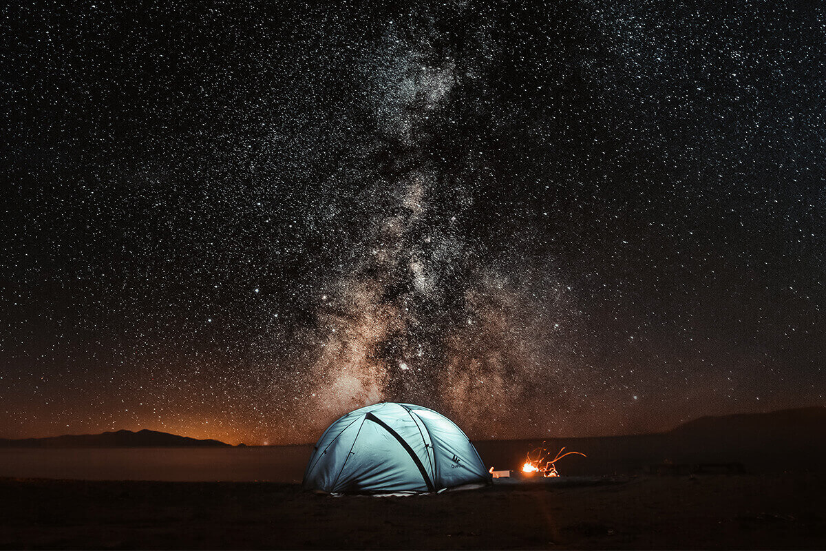 A tent set up on a cold night beside a campfire with the Milky Way overhead.