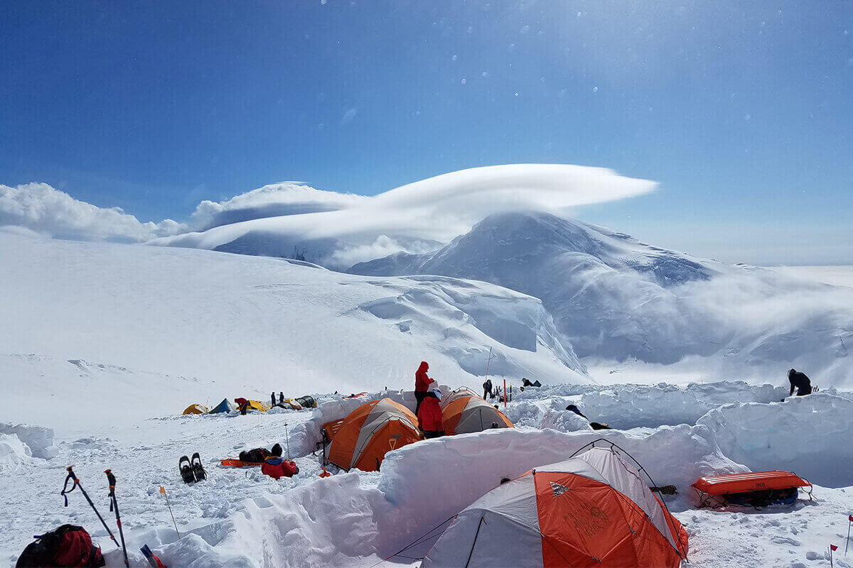 A snowy mountain scene where windbreaks made of snow protect 4-season tents from wintery winds.
