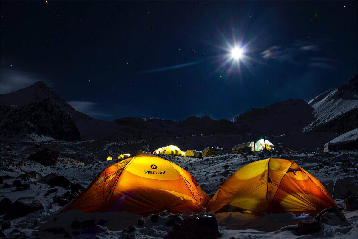 Tents set up on a snowy frozen landscape at the base of a mountain at night.