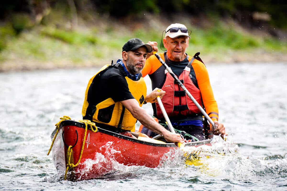 Two men wearing PFDs paddling a canoe on a river.