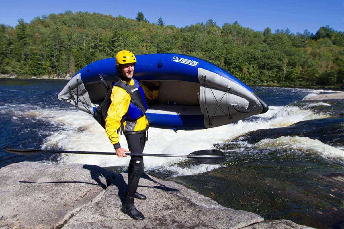 A kayaker carries an Explorer 300x alongside a whitewater river.