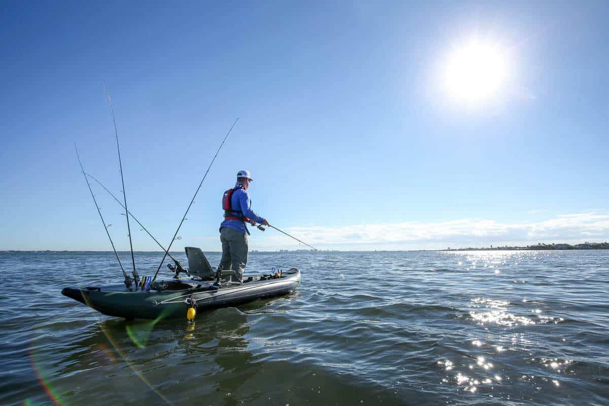 A fisherman on a lake stands and casts in a Sea Eagle 350fx Fishing Explorer.