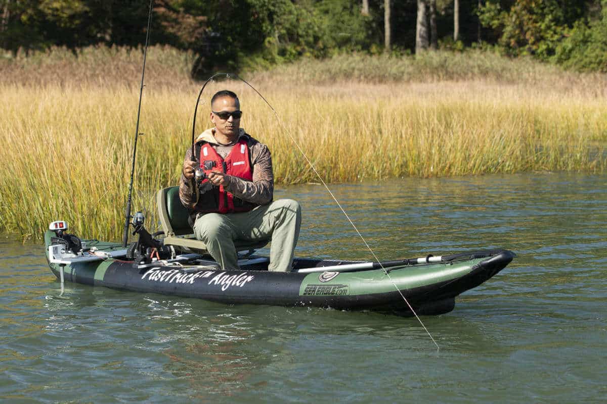A fisherman catches a fish from a Sea Eagle 385 FastTrack Angler inflatable kayak.