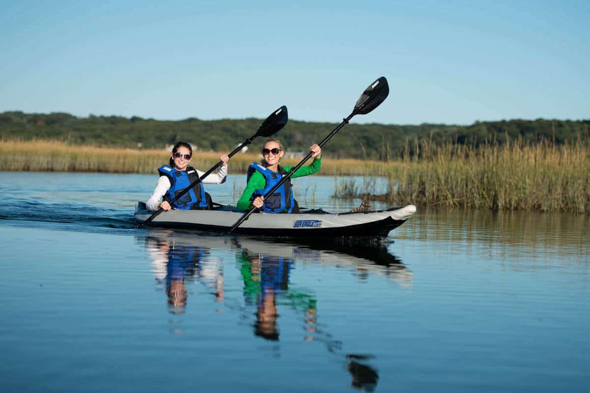 Two boaters tandem paddle a Sea Eagle 385ft FastTrack on a tranquil lake.