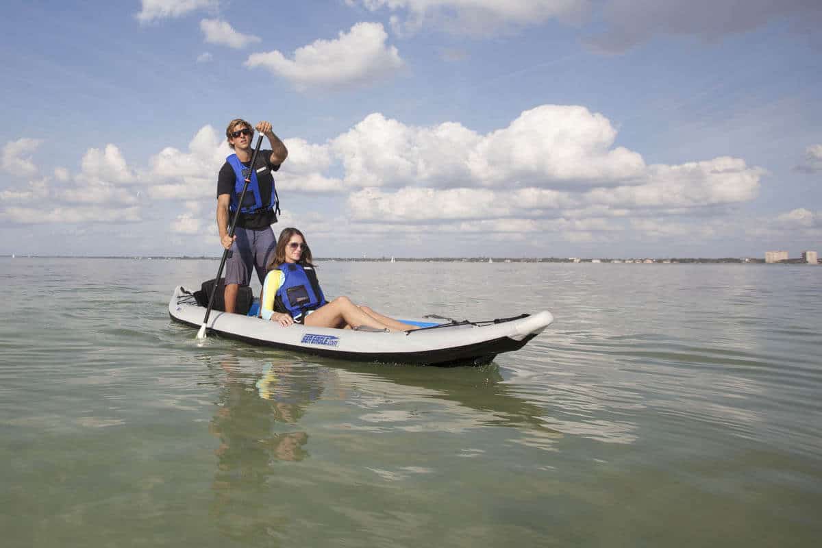 A boater stands in a FastTrack 385 and paddles with a SUP paddle while a female passenger reclines in the bow.
