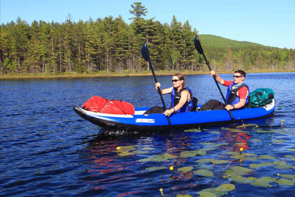 Two kayakers tandem paddle a Sea Eagle 420x loaded with gaming gear.