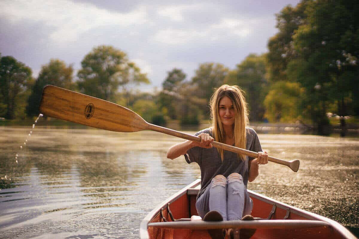 A woman canoeing on a lake with a wooden, single blade canoe paddle.