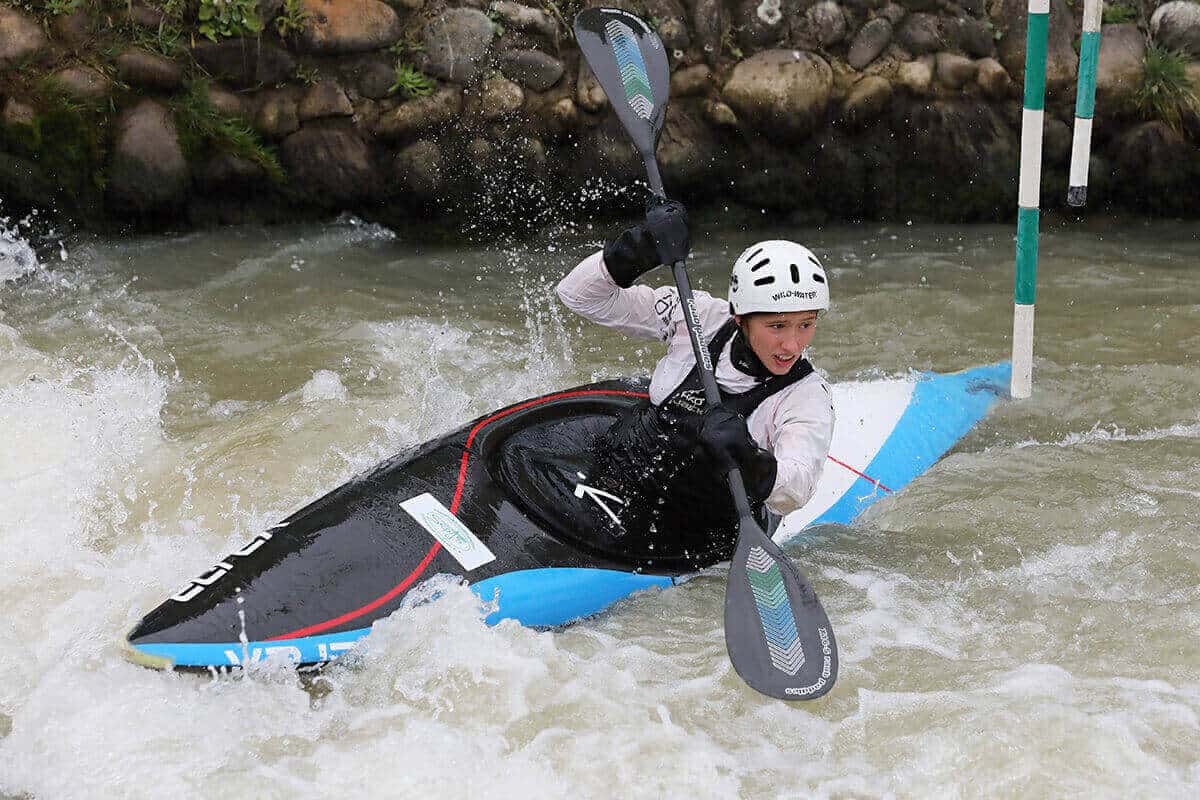 A whitewater slalom kayak being paddled through a watercourse.