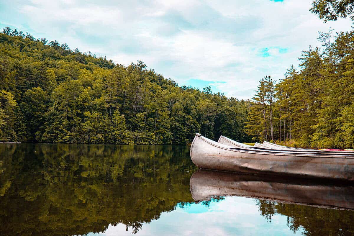 Aluminum canoes on a still water lake surrounded by woods.