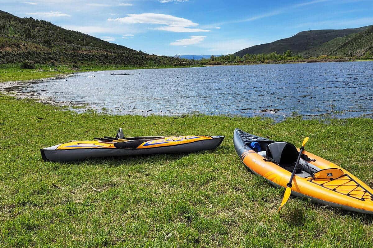 Two inflatable kayaks on a lake shore, an Aquaglide Deschutes 110 and the AdvancedFrame Sport Kayak.