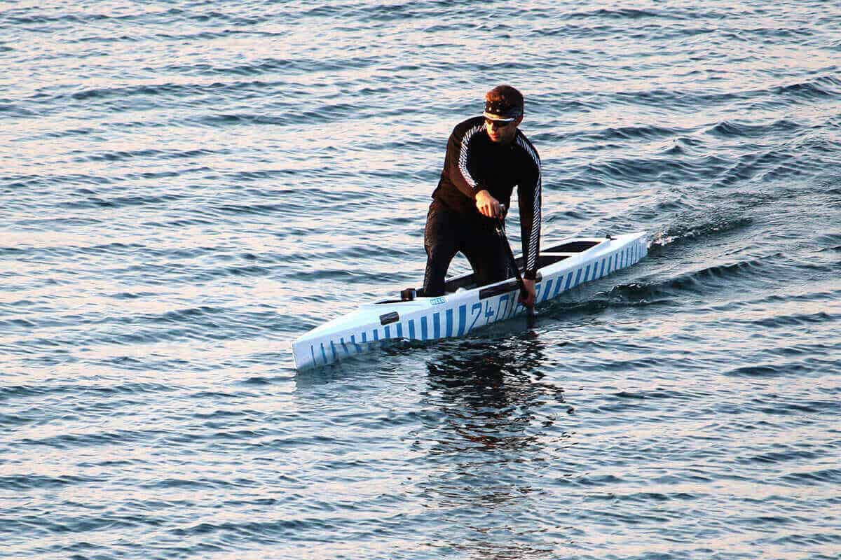 A man kneeling while paddling a racing canoe.