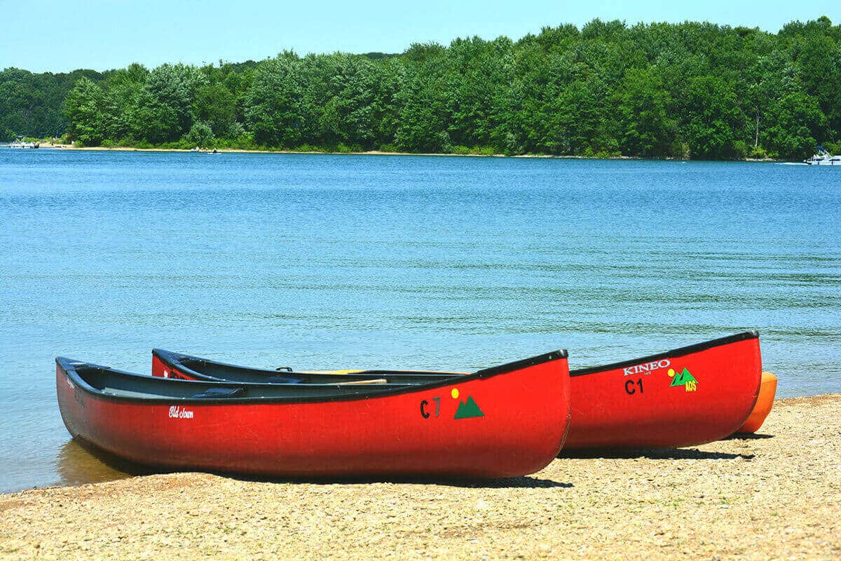 Two Old Town canoes and a kayak on the shore of a lake.
