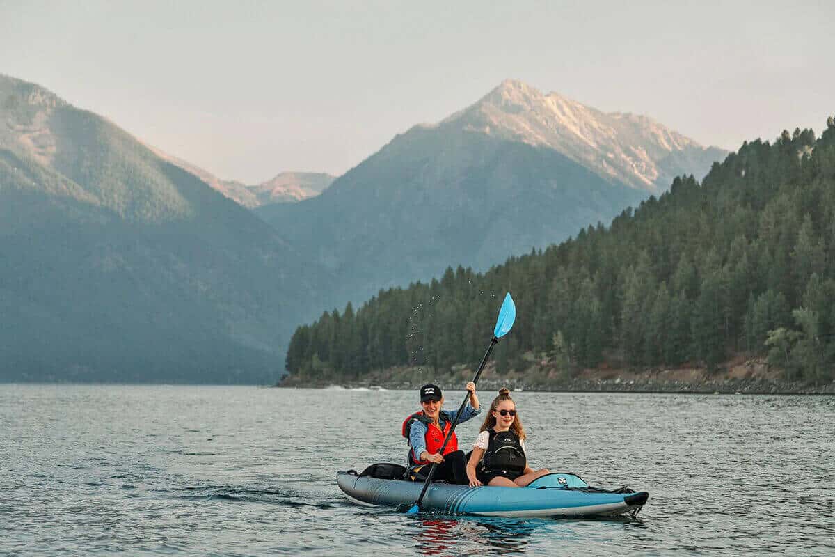 A tandem Aquaglide Chelan 155 inflatable kayak being paddled by a mother and daughter on a lake in the mountains.
