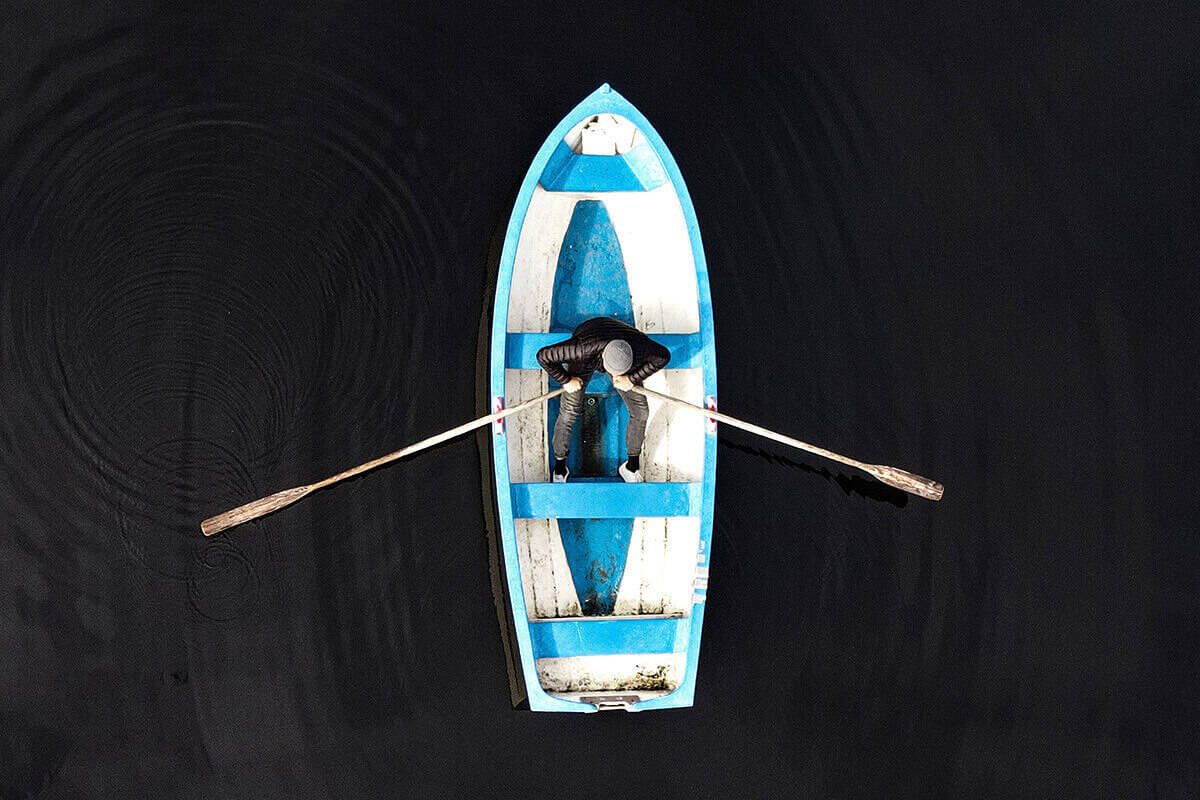 Man rowing a white and blue row boat.